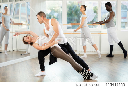 Pair of ballet dancers mastering supports during group rehearsal Pair of ballet dancers mastering supports during group rehearsal 115454333