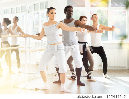 Concentrated Asian woman practicing demi plie at barre at ballet class 115454342
