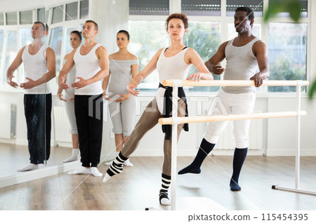 Ballerina performing battement tendu jete at ballet barre at group class 115454395