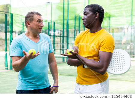 Men chatting on outdoor padel tennis court Men chatting on outdoor padel tennis court 115454468