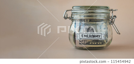 Glass jar full of American currency dollars cash banknote with text EMERGENCY. Preparation saving money. Moderate consumption and economy Glass jar full of American currency dollars cash banknote with text EMERGENCY. Preparation saving money. Moderate consumption and economy 115454942