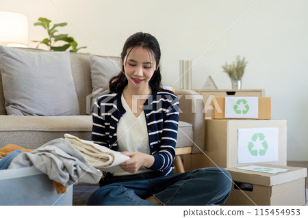 Young Woman volunteer to Recycle Clothes at Home, Sorting Donation for Charity, Promoting Sustainable Living and Environmental Responsibility 115454953