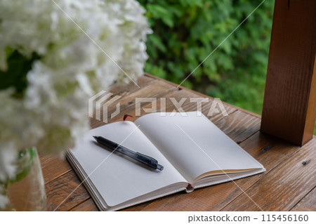 Empty white open paper notebook in wooden table outdoors in garden. Concept of self reflection discovery journal, writing gratitude 115456160