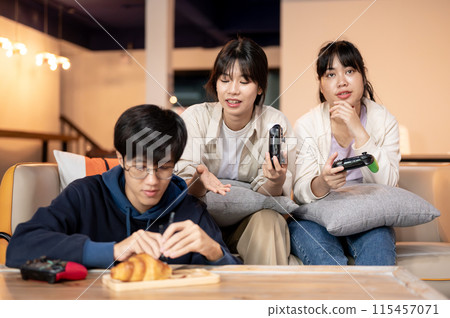A group of cheerful Asian friends are having a fun time together at home, playing video games. A group of cheerful Asian friends are having a fun time together at home, playing video games. 115457071