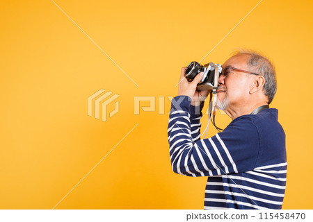 Portrait Asian old man wearing glasses look viewfinder vintage SLR camera studio shot isolated yellow background, smiling happy Photographer elderly man gray haired taking a picture of himself 115458470