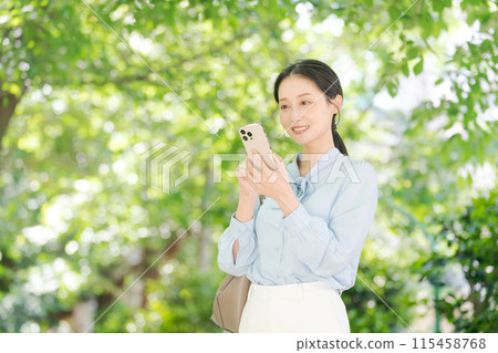 A woman looking at her smartphone among the fresh greenery A woman looking at her smartphone among the fresh greenery 115458768