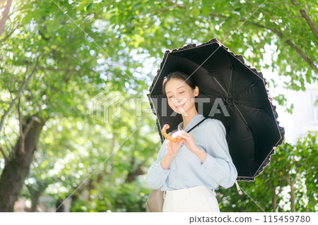 一個女人帶著陽傘走過新鮮的綠色植物 115459780