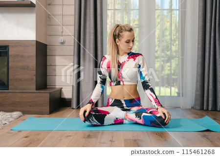 Woman in Colorful Leggings and Top Meditating on Blue Yoga Mat in Home Woman in Colorful Leggings and Top Meditating on Blue Yoga Mat in Home 115461268