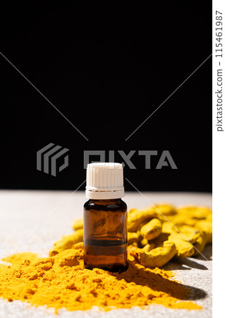 Turmeric essential oil in glass bottle among fresh turmeric and powder on black gray background. 115461987
