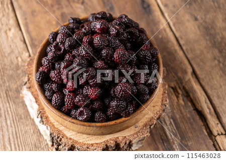 The black berry is a hybrid of raspberries and blackberries. Berries in a wooden bowl on the table. Vitamin summer food. Harvest. Raspberry and blackberry The black berry is a hybrid of raspberries and blackberries. Berries in a wooden bowl on the table. Vitamin summer food. Harvest. Raspberry and blackberry 115463028