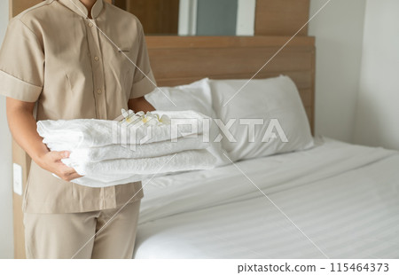 A hotel maid stacked towels on the bed and placed flowers on the towels in a hotel room 115464373