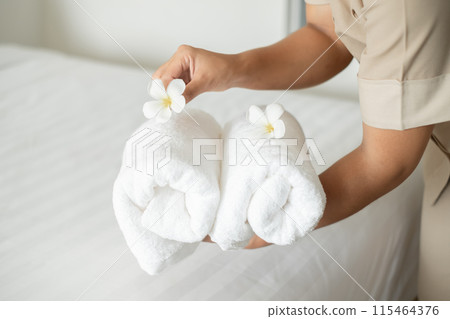A hotel maid stacked towels on the bed and placed flowers on the towels in a hotel room A hotel maid stacked towels on the bed and placed flowers on the towels in a hotel room 115464376