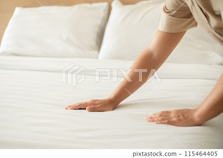 The hotel maid cleans and makes the bed in the hotel room The hotel maid cleans and makes the bed in the hotel room 115464405