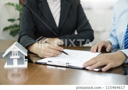 A real estate agent with a House model is talking to clients about buying home insurance. Home insurance concept A real estate agent with a House model is talking to clients about buying home insurance. Home insurance concept 115464617