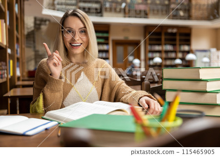 Cute blonde young woman studying in the library and looking excited Cute blonde young woman studying in the library and looking excited 115465905