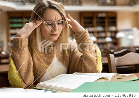 Blonde young woman studying in the library Blonde young woman studying in the library 115465916