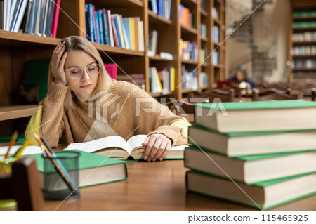 Blonde young woman studying in the library Blonde young woman studying in the library 115465925