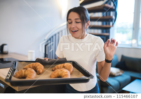 Dark-haired woman with a tray of fresh homemade croissants looking happy 115466107