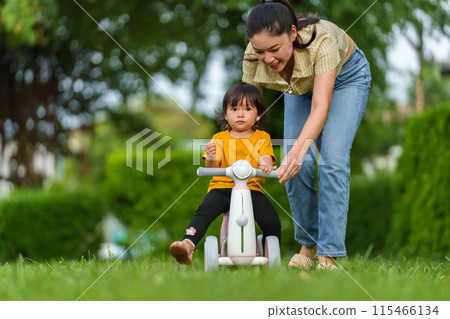 mother teaches her baby toddler girl rides plastic motorcycle toy in the park mother teaches her baby toddler girl rides plastic motorcycle toy in the park 115466134