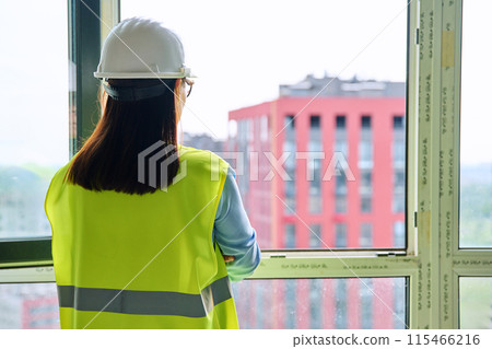 Back view of female industrial worker in protective helmet vest looking at new buildings Back view of female industrial worker in protective helmet vest looking at new buildings 115466216