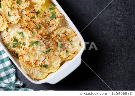 Potato gratin baked with cream and cheese on black slate background Potato gratin baked with cream and cheese on black slate background 115466988