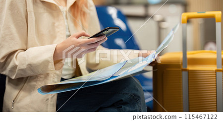 Young Woman at Airport with Luggage and Map, Using Smartphone for Travel Planning and Navigation, Modern Travel Concept, Solo Female Traveler, Exploring New Destinations, Travel Preparation 115467122