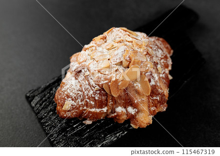 Almond croissant. puff pastry, delicate frangipane cream with almonds, enriched with butter. On top, the croissant has a hint of almond flakes and powdered sugar. on a black cutting board 115467319
