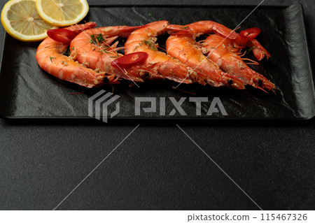 Large cooked king prawns on a black background. Lemon slices Large cooked king prawns on a black background. Lemon slices 115467326