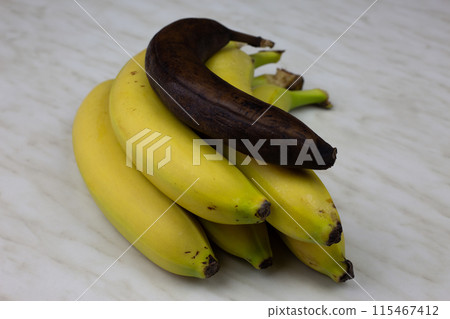 Bunch of bananas with one rotten banana. Overripe spoiled banana not suitable for eating lies on fresh juicy banana fruit, unhealthy eating with healthy food 115467412