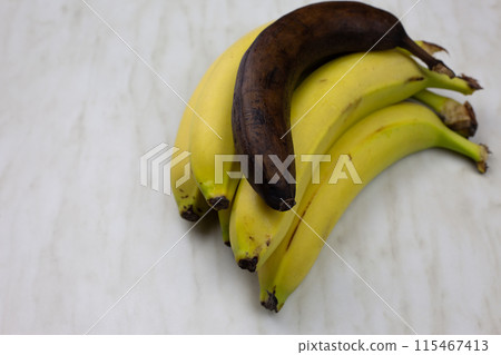 Rotten unhealthy banana fruit lies on fresh juicy bananas, spoiled overripe banana on white table 115467413