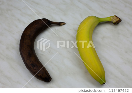 Black old banana next to fresh yellow banana. Spoiled fruit fruit on white table 115467422