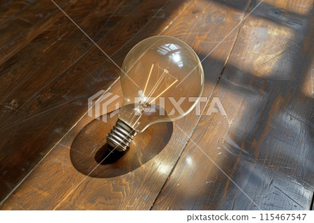 Vintage light bulb on a wooden floor with sunlight and shadows creating a warm atmosphere Vintage light bulb on a wooden floor with sunlight and shadows creating a warm atmosphere 115467547