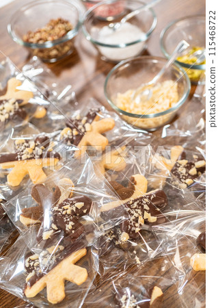 Carefully packaging Christmas cutout cookies, half-dipped in chocolate and presented in clear cellophane wrapping, perfect for festive gifting. Carefully packaging Christmas cutout cookies, half-dipped in chocolate and presented in clear cellophane wrapping, perfect for festive gifting. 115468722