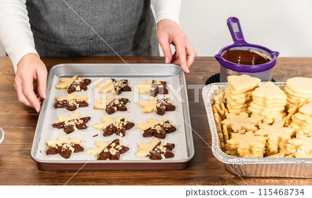 Creating cutout sugar cookies, partially dipped in chocolate and topped with hazelnut pieces, placed on parchment paper. 115468734