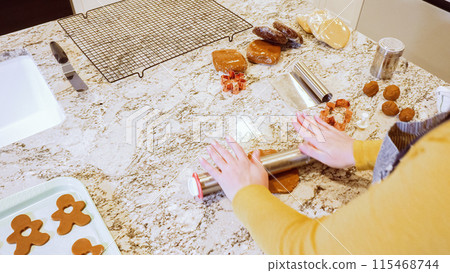 Using an adjustable rolling pin to roll out gingerbread cookie dough on the elegant marble counter in a modern kitchen, getting ready for festive holiday baking. 115468744