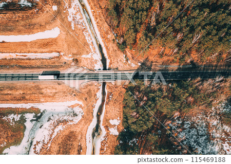 Aerial View Of Highway Road Through Spring Forest Landscape. Top View Of White Truck Tractor Unit Prime Mover Traction Unit In Motion On Freeway. Business Transportation, Trucking Industry. Flat View 115469188
