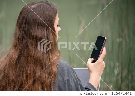 A woman is sitting on a dock with a laptop and a cell phone. She is talking on the cell phone while using the laptop. 115471441