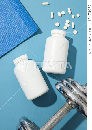 White plastic jars with pills and sport equipment on blue background, top view 115473082