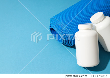 White plastic cans and yoga mat on blue background, space for text White plastic cans and yoga mat on blue background, space for text 115473084