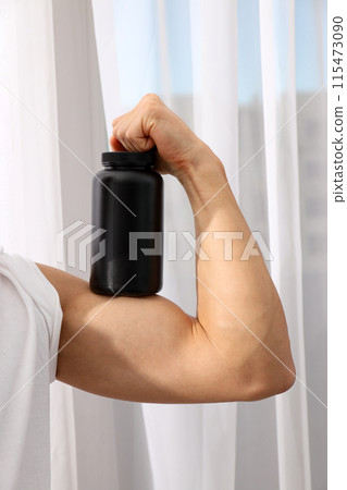 Black plastic jar on male biceps on light background Black plastic jar on male biceps on light background 115473090