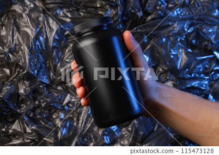 Black plastic jar in male hand on dark background Black plastic jar in male hand on dark background 115473128