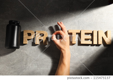 Black plastic jar, wooden letters and male hand on dark gray background, top view Black plastic jar, wooden letters and male hand on dark gray background, top view 115473137