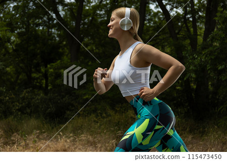 Strong athletic woman in sportswear with headphones running outdoors Strong athletic woman in sportswear with headphones running outdoors 115473450