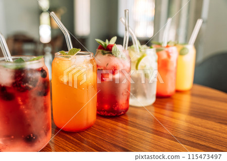 Fruit drinks with berries and ice in glass glasses and straws on a wooden table 115473497