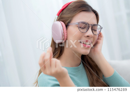 Happy young woman wearing headphones listening music while sitting on sofa with fun and enjoy. Happy young woman wearing headphones listening music while sitting on sofa with fun and enjoy. 115476289