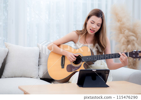 Young asian woman sitting on sofa looking tablet for practice music with guitar in living room. Young asian woman sitting on sofa looking tablet for practice music with guitar in living room. 115476290
