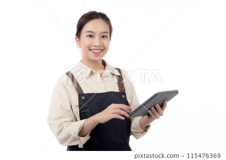 Portrait happy young asian barista woman in apron smiling while using digital tablet isolated. Portrait happy young asian barista woman in apron smiling while using digital tablet isolated. 115476369