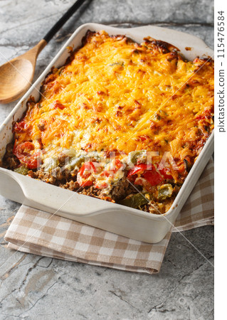 John Wayne Casserole is a delicious taco beef casserole cooked in biscuit dough with sour cream, Cheddar cheese, tomatoes, and bell peppers closeup on the baking dish. Vertical 115476584