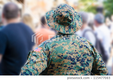 American soldier in a tactical panama view from the back. Chevron with the American flag on the sleeve of a green pixelated military uniform American soldier in a tactical panama view from the back. Chevron with the American flag on the sleeve of a green pixelated military uniform 115477083