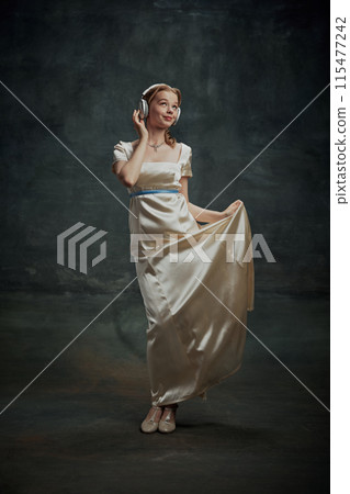 Portrait of elegant beautiful young woman in silk dress, royal person listening to music in headphones against dark vintage green background 115477242
